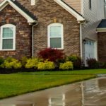 Power washing technician applying sealer to a concrete driveway in front of a brick home