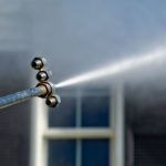 Power washing technician using safe pressure to wash white vinyl siding
