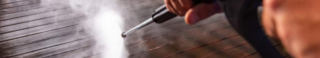 Up-close shot of power washing wand being used to wash floor of a wooden deck