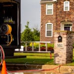 Hydro Savage Pressure Washing truck in cul-de-sac in front of brick and vinyl home with two technicians working in the distance