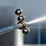 Power washing wand spraying white vinyl siding at a safe pressure to remove dirt and algae