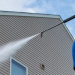 Power washing technician using soft wash process to remove contaminants from tan vinyl siding