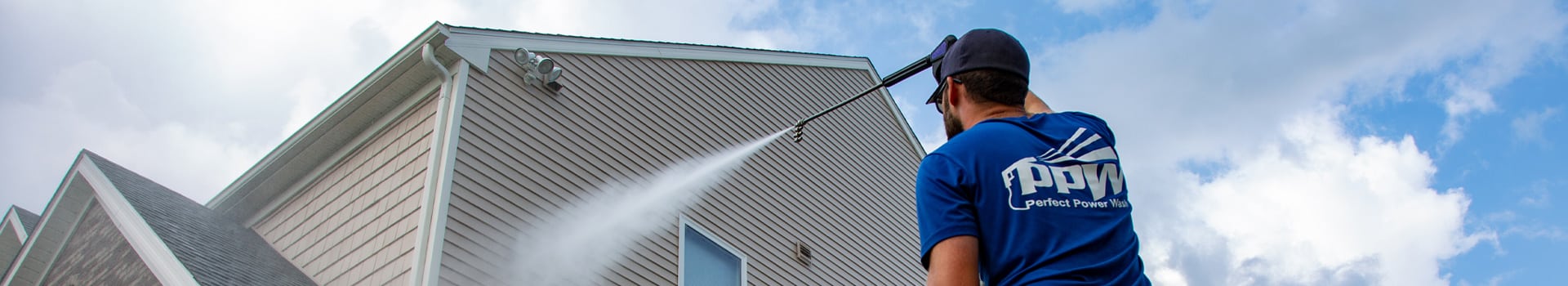 Power washing technician using soft wash process to remove contaminants from tan vinyl siding