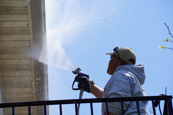 Power washing technician using safe pressure to remove contaminants from white vinyl siding