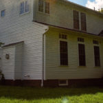 Power washing technician using safe pressure to wash the exterior of a home with yellow vinyl siding