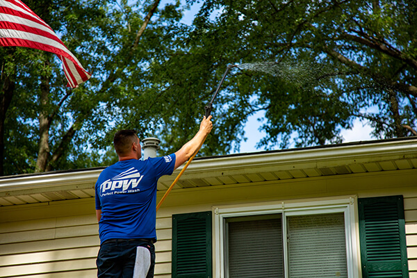 Power washing technician using very low pressure to safely treat a roof for streaking and moss