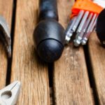 Just a few of the 21 tools every homeowner should have, including as a hammer, screwdriver, and measuring tape, set on the surface of a wooden deck