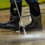 Power washing technician using safe pressure on a concrete driveway using a wand